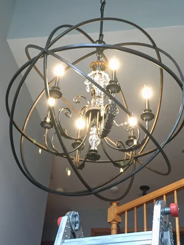 Ornate orb chandelier installation in progress, work ladder in frame